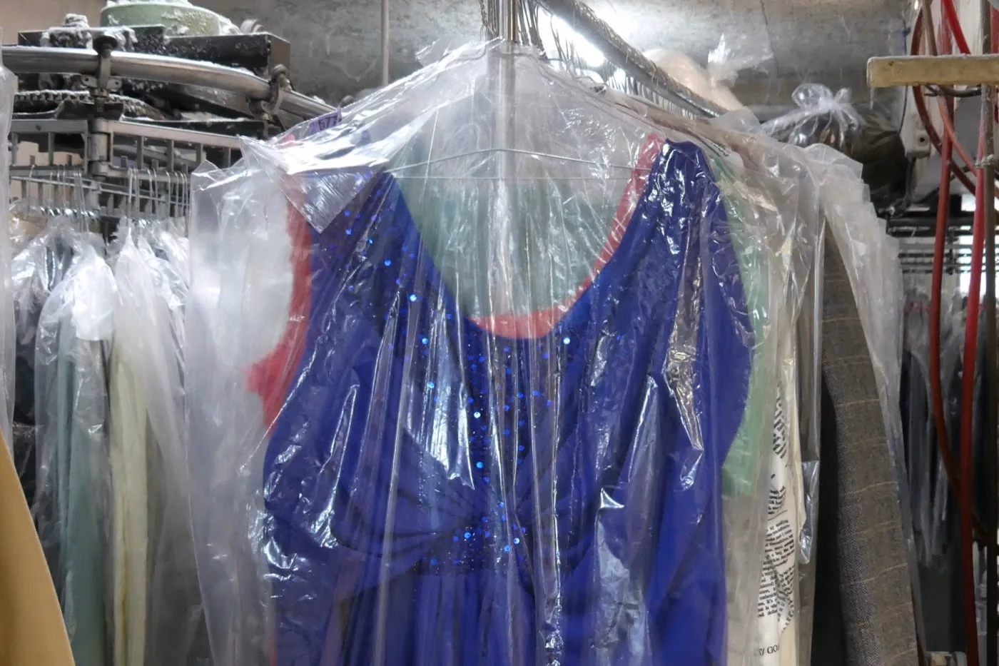 Vêtements protégés sous housse sur le convoyeur du Pressing Belle Allure