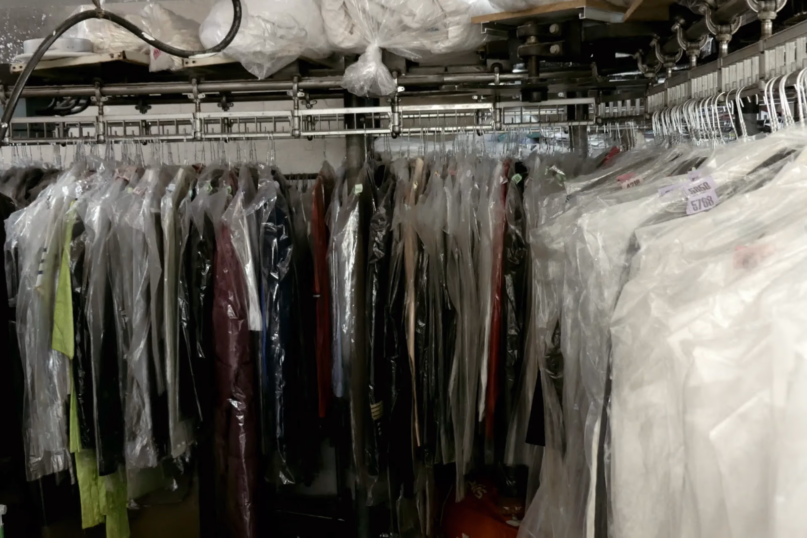 Portants de vêtements sous housse dans l'atelier du Pressing Belle Allure